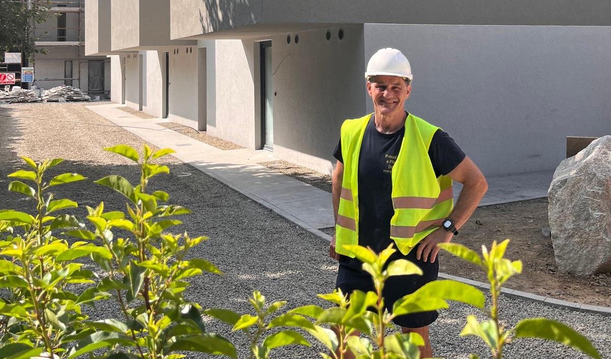 Mel Reynolds in a hi-vis vest and hard hat standing on site in front of a row of newly rendered homes.